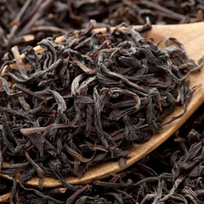 Wooden spoon with black tea leaves on a background of more tea leaves